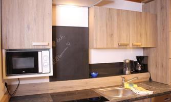 A modern kitchen with wooden cabinets and a black refrigerator. On the countertop, there is a microwave, a coffee machine, and a sink.