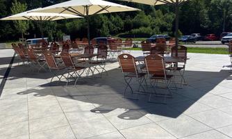 A terrace with wooden chairs and large umbrellas. In the background, trees and blue sky are visible.