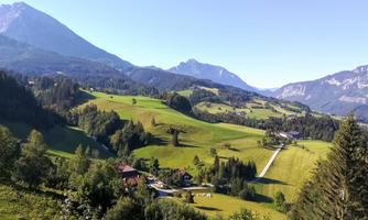 A picturesque landscape with gentle hills and green meadows. In the background, impressive mountains and a clear blue sky can be seen.