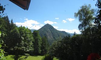 A picturesque landscape with a mountain in the background. In the foreground, there are green trees and a meadow, under a clear blue sky.