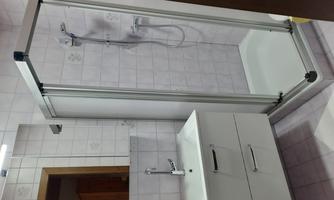 A modern bathroom with a shower cubicle and a sink. The walls are brightly tiled, and the furnishings are simple and functional.