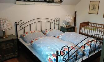 A cozy bedroom with a double bed and a children's bed. The bed linen is adorned with blue checks and colorful floral patterns.