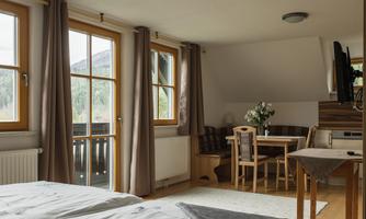 A cozy room with a double bed, a table, and chairs. Large windows with a view of nature and soft colors in the room.