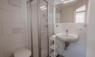 A modern bathroom with a shower, a sink, and a toilet. It is designed in bright colors and appears clean and functional.