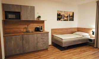 A modern accommodation with a small kitchen and a sleeping area. The room is bright and inviting, with wooden flooring and simple furniture.