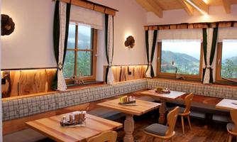 A cozy restaurant with wooden furniture and large windows. The view showcases a beautiful landscape with mountains and trees.