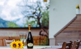 A beautiful table outdoors with a bottle of champagne and glasses. On the table lies a sunflower, surrounded by a green tablecloth.