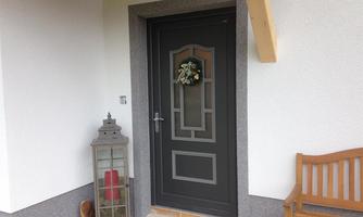 A black front door with a wreath and a lantern beside it. Next to the door is a wooden bench.