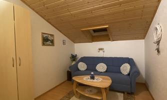 A cozy living space with a blue sofa and a wooden table. The walls are light, and the ceiling has wood paneling.