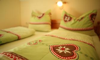 A cozy bedroom with a double bed and colorful bedspreads. The covers are green with heartfelt patterns and complement the warm atmosphere of the room.