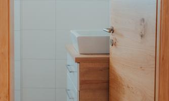 A modern bathroom with bright tiles and a wooden cabinet. The sink area is well-lit and tidy.