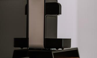 A modern coffee machine is on a wooden table. In the background, a flat-screen television can be seen.