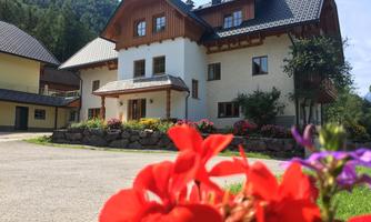 A beautiful house in alpine style surrounded by flowers. In the background, mountains and a blue sky can be seen.