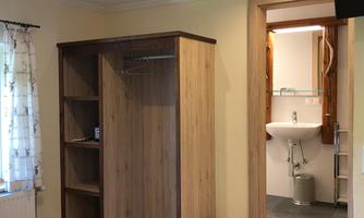 A simple room with a wooden wardrobe and access to the bathroom. The room has a bright atmosphere with a combination of wooden and tiled flooring.