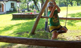 A little boy is happily swinging on a swing in a park. In the background, trees and a cozy seating area can be seen.