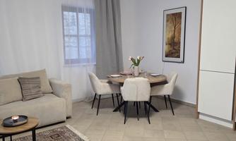 A modern living room with a cozy sofa and a round dining table. The room is bright and welcoming with friendly colors and a decorative wall design.