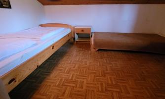 A simple room with two beds and a nightstand. The floor is made of hardwood parquet.