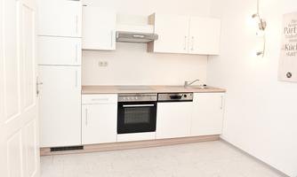 A modern, bright kitchen with white cabinets and a wooden countertop. There is an oven, a stove, and a sink, as well as minimalist lighting.