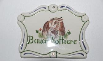 A decorative ceramic sign with the inscription "Farm Animals." It features a drawing of animals and is adorned with colorful details.