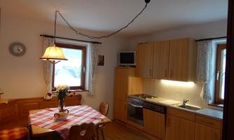 A cozy kitchen with a dining table and wooden furniture. The walls are light, and there are windows that provide natural light.