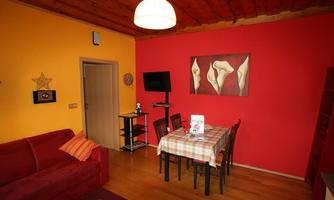 A cozy living room with a red wall and a yellow wall. A dining table with chairs and a red sofa can also be seen.