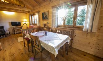 A cozy dining area in a wooden apartment with a table and chairs. Sunlight streams through the windows, creating a warm atmosphere.