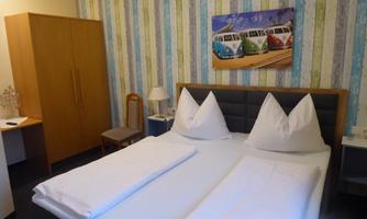 A cozy room with a double bed and stylish cushions. The walls are striped, and a colorful picture of VW buses hangs above the bed.