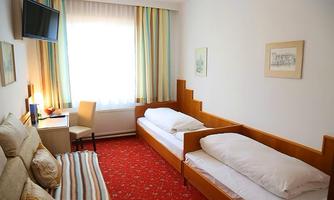 A simple room with two single beds and a television. Bright curtains and a cozy ambiance create a pleasant atmosphere.