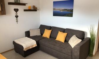 A cozy living room with a gray sofa and orange cushions. A picture of a cityscape over water hangs on the wall.
