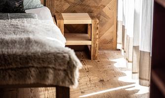 A cozy bedroom with a wooden floor and a small nightstand. Soft textiles and natural lighting create an inviting atmosphere.