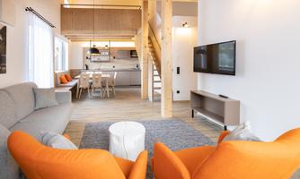 A modern living room with a bright, open space concept. The orange armchairs and the wooden table give the setting an inviting atmosphere.