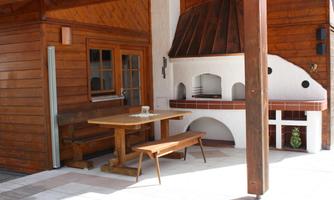 A cozy terrace with a wooden table and benches. In the background, there is a grill with a rustic design.