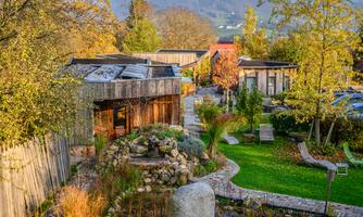 A beautiful garden with modern wooden houses and a small pond. Trees and shrubs create a tranquil atmosphere in the surroundings.