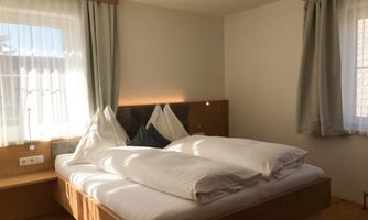 A cozy bedroom with a large double bed and light curtains. The walls are in neutral colors and provide a calm atmosphere.