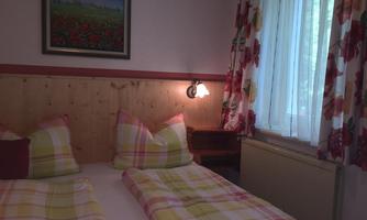 A cozy bedroom with two beds and colorful bedding. Natural light flows through the window, and a painting decorates the wall.