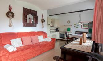 A cozy living room with a red sofa and a dining table. The kitchen is open and well-equipped.