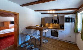 A modern kitchen with wooden details and elegant bar stools. The space is bright and friendly designed, featuring a dining area and modern appliances.