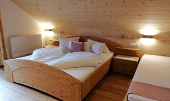 A cozy bedroom with a large wooden bed and soft lighting. There is also an additional bed and wooden details that create a warm atmosphere.