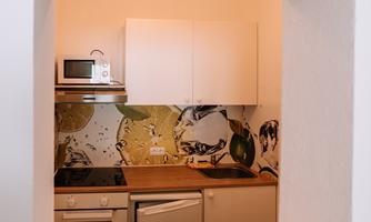 A modern view of a kitchen through a large wall window. The walls are adorned with decorative wallpaper and a wooden surface featuring a red flower.