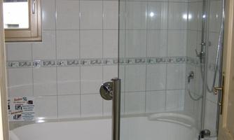 A modern bathroom with a shower and a bathtub. The walls are brightly tiled and there is a window for natural light.