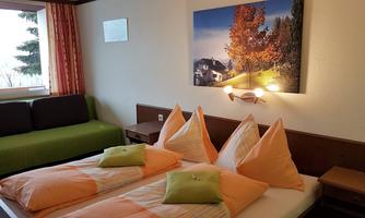A cozy hotel room with two beds and colorful cushions. In the background, there is a picture of an autumn landscape.