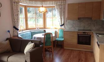 A bright living space with a modern kitchenette and a cozy dining area. The windows provide a view outside and are decorated with curtains.