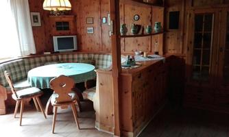 A cozy dining area with a round tablecloth and a built-in bench. Wooden furniture and a warm atmosphere characterize the room.