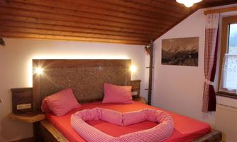 A cozy bedroom with a large bed and wooden walls. The bedding is red checked and there is soft lighting.