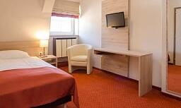 A simple hotel room with a double bed and a small table. There is a television and a mirror on the wall.