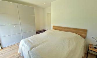 A cozy bedroom with a large bed and a modern wardrobe. The walls are bright and the floor is made of wood.