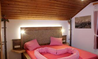 A cozy bedroom with a double bed and romantic heart-shaped pillows. The wooden wall paneling and the decorations create an inviting atmosphere.