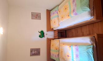 A simple bedroom with two single beds and colorful bedcovers. Pictures and a decorative wall figure hang on the walls.