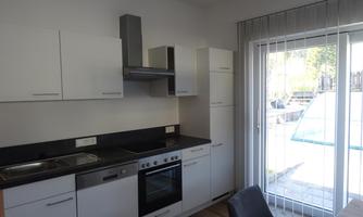 A modern kitchen with white cabinets and a black countertop. A large window view of a terrace is also visible.