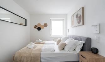 A modern bedroom with a large bed and cozy pillows. The walls are bright and adorned with artistic decorations.